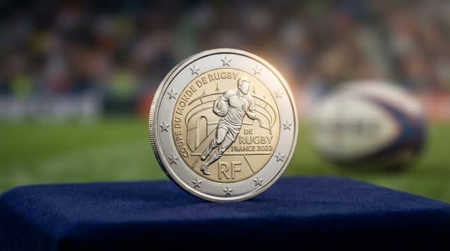 Close-up of a French 2 Euro Rugby World Cup 2023 coin with a player design, on blue velvet, blurred stadium background.