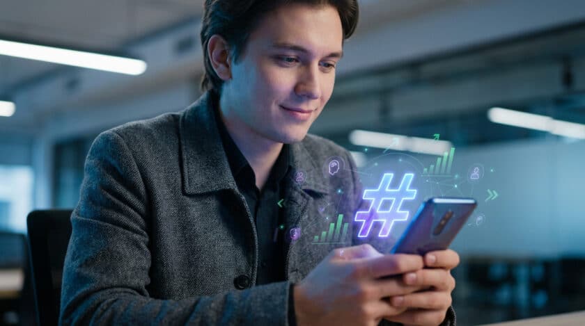 Jeune homme utilise son smartphone, affichant un hashtag lumineux entouré d'icônes de croissance et de réseau, symbolisant l'analyse des médias sociaux.